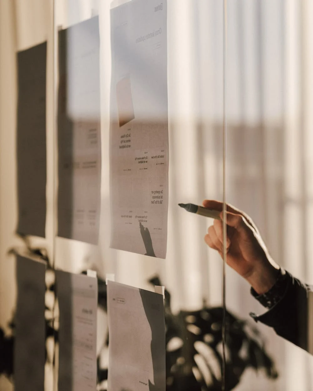 A hand with a marker pointing at strategy pages pinned to a glass wall